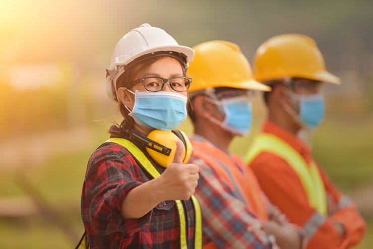 Woman wearing PPE gives thumbs up in warehouse