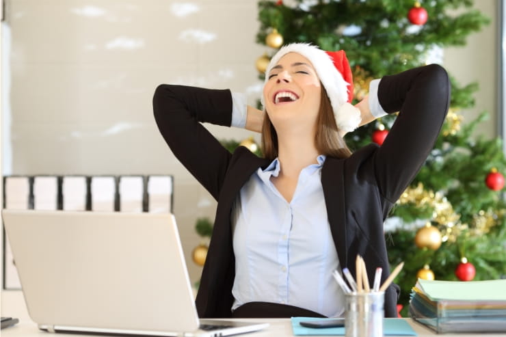 woman laughing in front of computer with a christmas hat and a christmas tree at the back