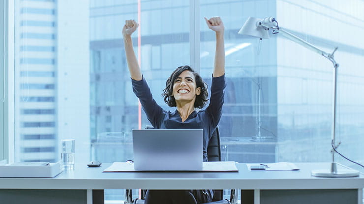 Person at desk with arms raised in triumph