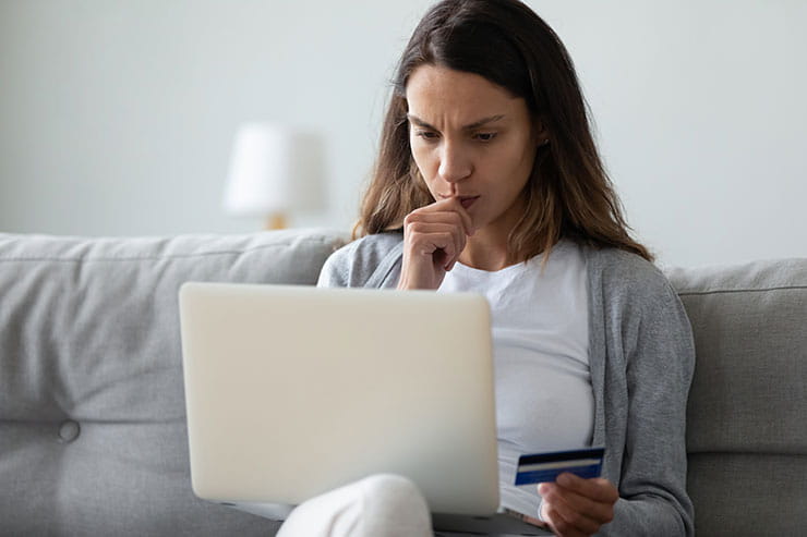 Femme à l’air inquiet, carte de crédit en main, devant un ordinateur portable.