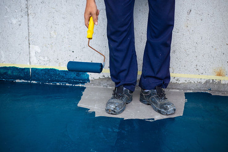 Une personne qui tient un rouleau à peinture a peint le sol autour de ses pieds : Les erreurs commises au travail.