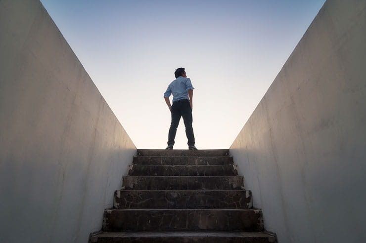 Person stands at top of underground staircase, looking at sky