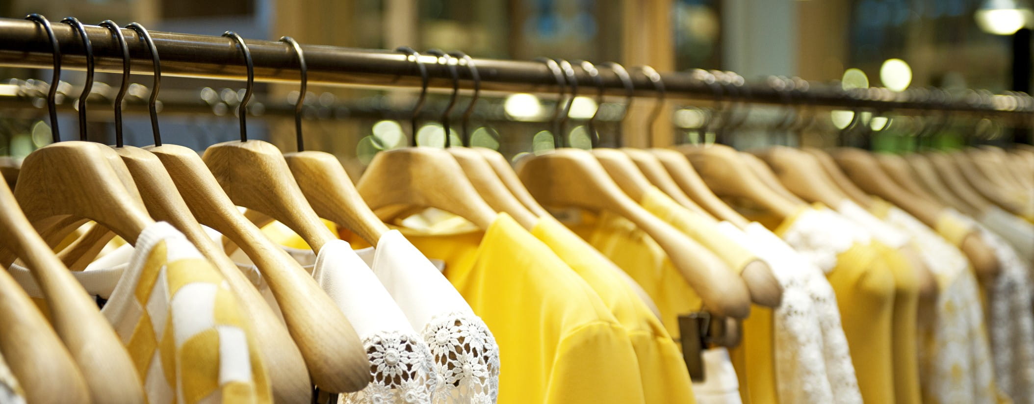 Yellow and white clothes hang on wood hangers, tightly packed on a clothing rack 